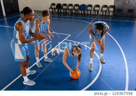 Female basketball players training, one doing push-ups with ball on court 120367398