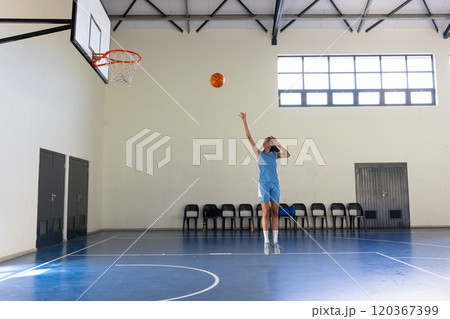 Playing basketball, woman shooting ball towards hoop in indoor court, copy space 120367399