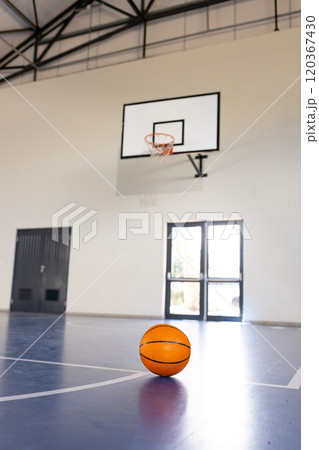 Basketball on court in gymnasium with hoop in background, ready for game, copy space 120367430