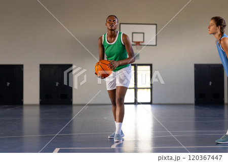 Playing basketball, woman in green jersey preparing to shoot ball in gym 120367447