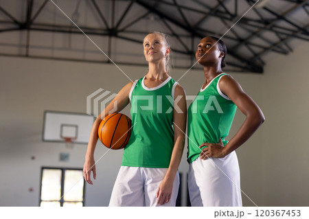 Holding basketball, two female basketball players posing confidently in gym Holding basketball, two female basketball players posing confidently in gym 120367453