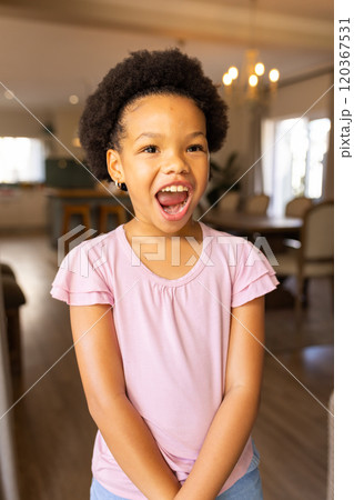Smiling girl in pink shirt standing in living room, expressing joy and excitement Smiling girl in pink shirt standing in living room, expressing joy and excitement 120367531