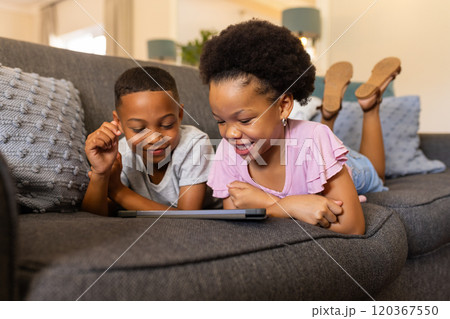 brother and sister lying on couch, watching tablet and smiling, enjoying time together 120367550