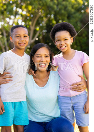 Smiling mother hugging her two brother and sister, enjoying time together outdoors 120367580