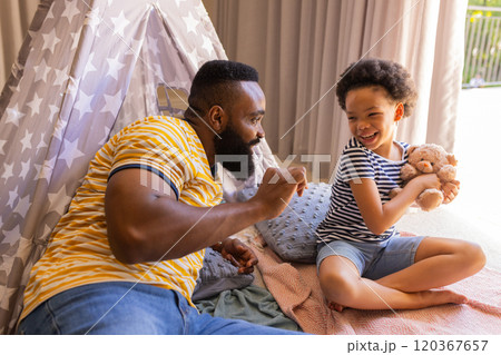 Playing with stuffed animal, father and daughter enjoying quality time indoors, in teepee 120367657