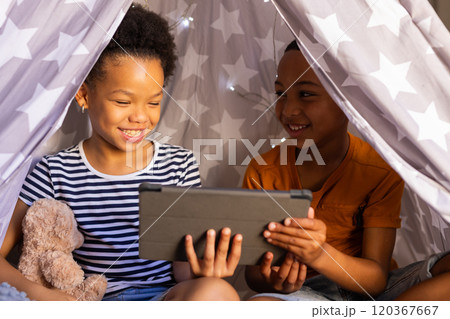 Under blanket fort, brother and sister playing together using tablet, smiling and enjoying time, in Under blanket fort, brother and sister playing together using tablet, smiling and enjoying time, in 120367667