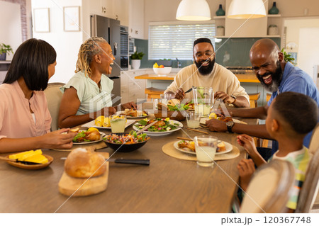multigenerational family enjoying meal together, laughing and sharing food at dining table 120367748
