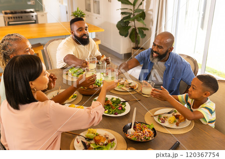 multigenerational family enjoying dinner together, raising glasses for toast at home 120367754
