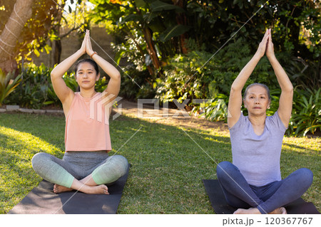 Practicing yoga, asian grandmother and granddaughter sitting on mats in garden, meditating together Practicing yoga, asian grandmother and granddaughter sitting on mats in garden, meditating together 120367767