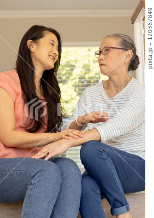 Smiling asian grandmother and granddaughter, holding hands and sitting together 120367849