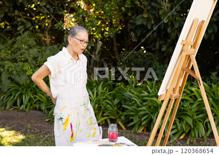 Painting on canvas, elderly asian woman in apron focusing on her artwork outdoors 120368654