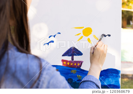 Creating colorful seascape, woman painting on canvas outdoors 120368679