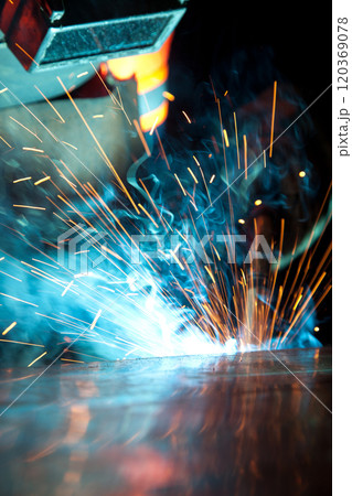Welder uses torch to make sparks during manufacture of metal equipment, industrial professional worker 120369078