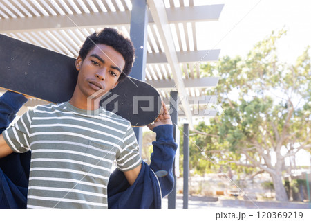 Holding skateboard, african american teenage boy in striped shirt hanging out outdoors 120369219