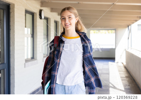 Smiling teenage girl carrying books and backpack, walking in school hallway Smiling teenage girl carrying books and backpack, walking in school hallway 120369228