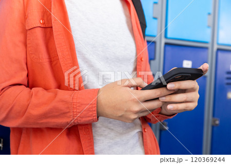 Using smartphone, teenage girl standing by lockers in school, wearing orange jacket Using smartphone, teenage girl standing by lockers in school, wearing orange jacket 120369244