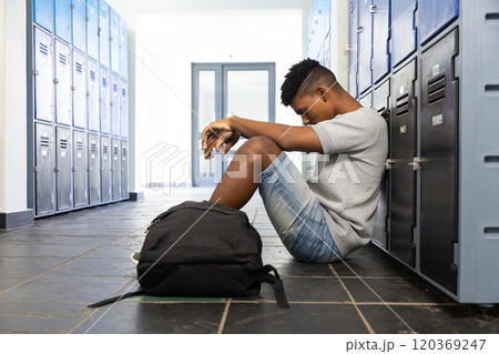 Sitting in school hallway, teenage boy leaning against lockers with backpack Sitting in school hallway, teenage boy leaning against lockers with backpack 120369247