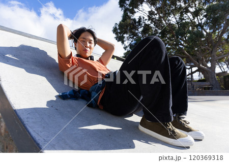 Relaxing on skateboard ramp, Asian teenage boy enjoying sunny day outdoors Relaxing on skateboard ramp, Asian teenage boy enjoying sunny day outdoors 120369318