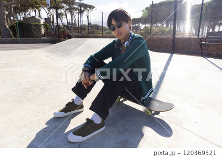 Outdoors, Sitting on skateboard, asian teenage boy relaxing at skate park in casual outfit Outdoors, Sitting on skateboard, asian teenage boy relaxing at skate park in casual outfit 120369321