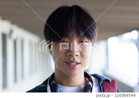 Asian teenage boy with headphones smiling confidently in school hallway, enjoying break Asian teenage boy with headphones smiling confidently in school hallway, enjoying break 120369344