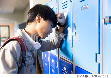 Leaning against locker, stressed asian teenage boy in school hallway 120369353
