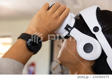 Using VR headset, asian teenage boy exploring virtual reality experience in school setting 120369375