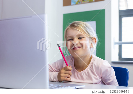 Smiling girl holding pencil and using laptop in school classroom Smiling girl holding pencil and using laptop in school classroom 120369445