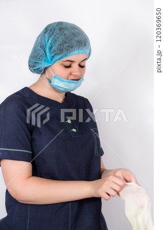 A young nurse in a medical cap and mask and putting on rubber gloves 120369650