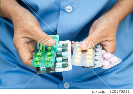 Asian senior woman patient holding antibiotics capsule pills for treatment infection patient in hospital, Pharmacy drugstore. Asian senior woman patient holding antibiotics capsule pills for treatment infection patient in hospital, Pharmacy drugstore. 120370231