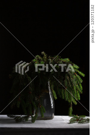 A transparent vase with green fluffy branches of a Christmas tree stands on the table 120371182
