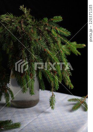 A transparent vase with green fluffy branches of a Christmas tree stands on the table 120371185
