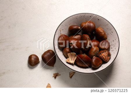 Delicious edible chestnuts in a small bowl on a white table Delicious edible chestnuts in a small bowl on a white table 120371225