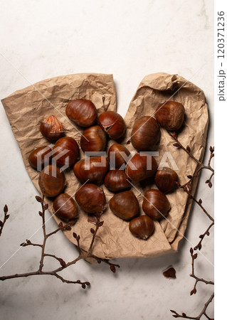 Fresh harvest of edible chestnuts scattered on a on kraft paper with tree branches 120371236