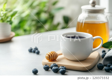 Tea setup with a white cup of blueberry tea, honey dipper, blueberries, and a teapot Tea setup with a white cup of blueberry tea, honey dipper, blueberries, and a teapot 120373332