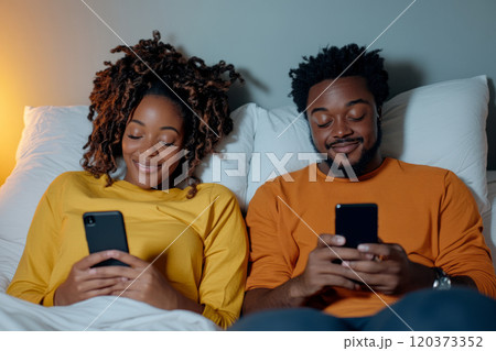 Happy couple lying in bed, smiling while using smartphones 120373352