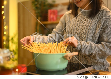 Smiling woman dressed in gray sweater preparing pasta in a holiday decorated kitchen Smiling woman dressed in gray sweater preparing pasta in a holiday decorated kitchen 120373414