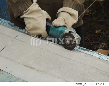 A builder wearing construction gloves cuts or carves metal sheet with a grinder A builder wearing construction gloves cuts or carves metal sheet with a grinder 120373416