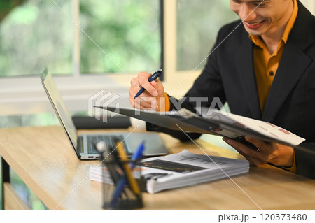 Professional businessman in black suit reviewing documents at desk 120373480