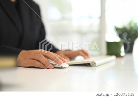 Close up of employee hand on computer mouse and keyboard in office workspace Close up of employee hand on computer mouse and keyboard in office workspace 120373519