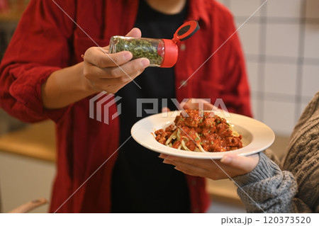 Cropped shot of man sprinkling herbs on spaghetti bolognese before serving Cropped shot of man sprinkling herbs on spaghetti bolognese before serving 120373520