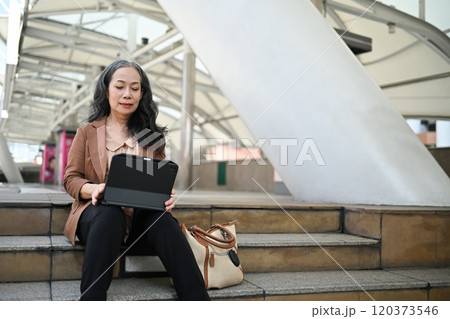 Beautiful mature businesswoman using digital tablet on steps in public space Beautiful mature businesswoman using digital tablet on steps in public space 120373546