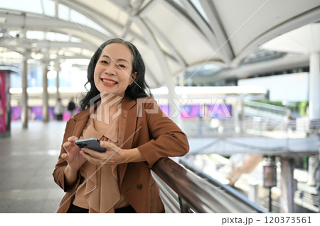 Cheerful mature businesswoman using smartphone in modern urban area 120373561