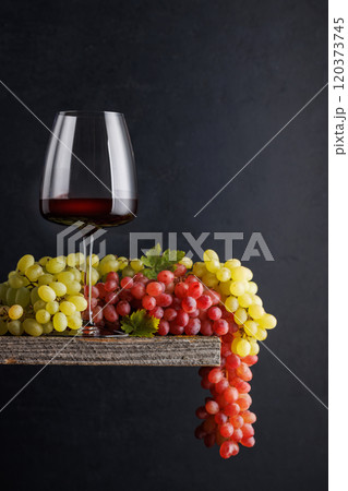 A glass of wine paired with grapes, set against a dark background 120373745