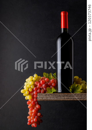 A bottle of wine paired with grapes, set against a dark background 120373746