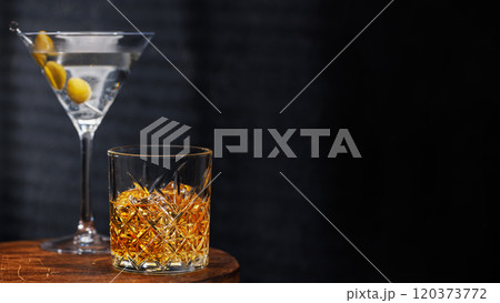 A whiskey glass and martini cocktail resting on a wooden table, set against a dark background A whiskey glass and martini cocktail resting on a wooden table, set against a dark background 120373772