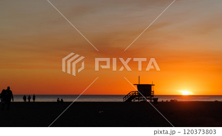 Los Angeles beach at sunset, featuring a lifeguard tower silhouette against a glowing orange and purple horizon 120373803