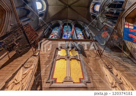 The Chancel of St. Patrick's Cathedral in Dublin features a large mosaic cross, flanked by military regimental flags and stone carvings. Above, the gothic stained glass windows add a solemn atmosphere 120374181
