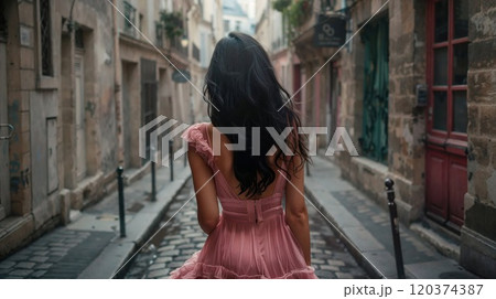 Romantic view from behind of woman in pink flowing dress walking through charming narrow cobblestone street in Paris. Vintage style urban photography with European architecture 120374387