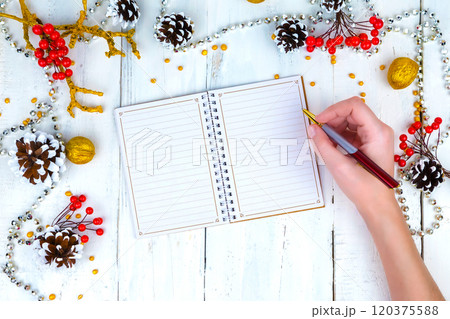Christmas wooden background with cones and notepad. The hands that write in the notebook. Christmas wooden background with cones and notepad. The hands that write in the notebook. 120375588