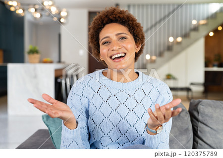 Smiling woman in blue sweater gesturing while sitting on couch at home, on video call Smiling woman in blue sweater gesturing while sitting on couch at home, on video call 120375789